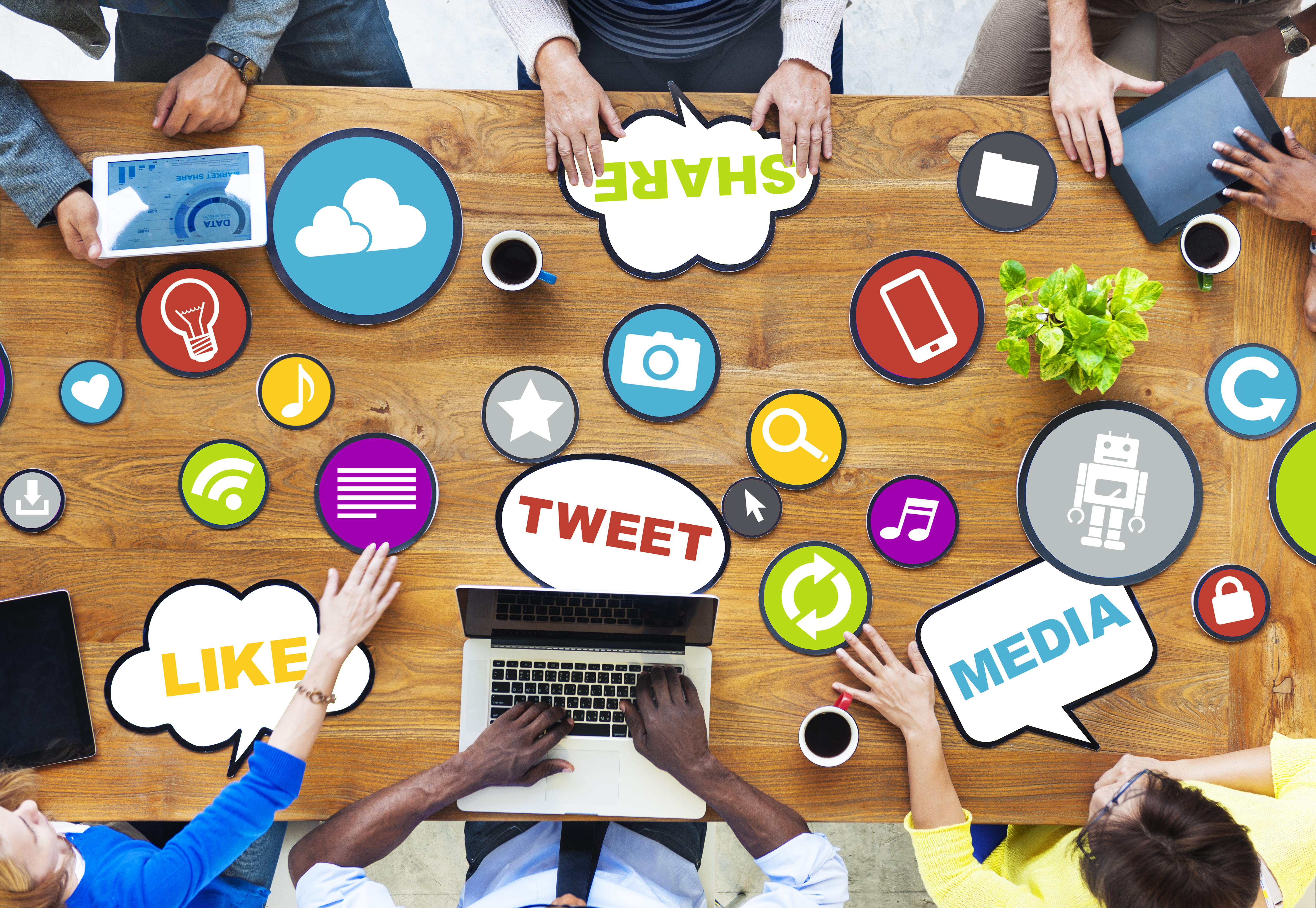 People around table with laptops and tablets with social media icons strewn around table top